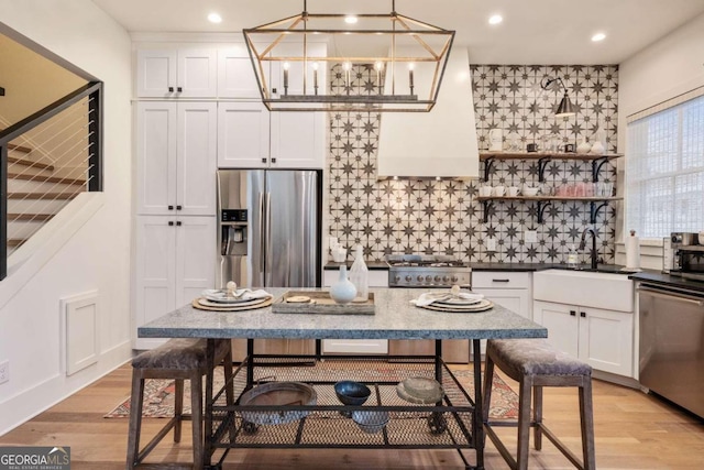 kitchen with sink, white cabinetry, light wood-type flooring, appliances with stainless steel finishes, and pendant lighting