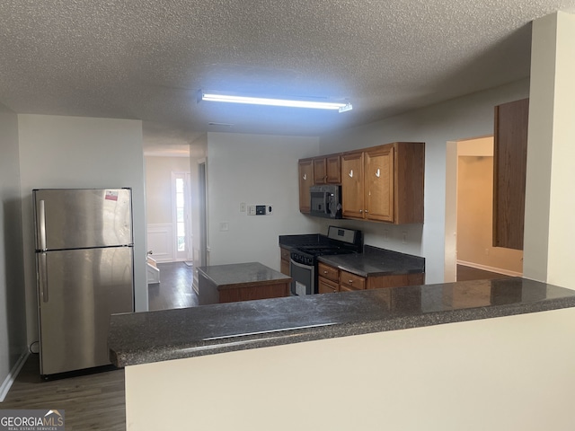 kitchen featuring kitchen peninsula, dark wood-type flooring, a textured ceiling, and appliances with stainless steel finishes