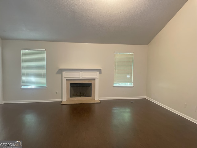 unfurnished living room with vaulted ceiling, a textured ceiling, a wealth of natural light, and dark wood-type flooring