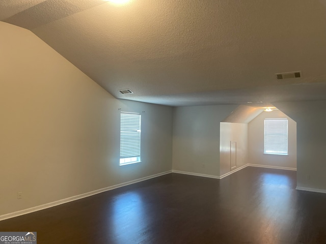 bonus room featuring a wealth of natural light, lofted ceiling, dark wood-type flooring, and a textured ceiling