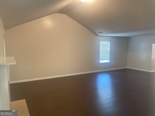 spare room featuring a textured ceiling, dark wood-type flooring, and lofted ceiling