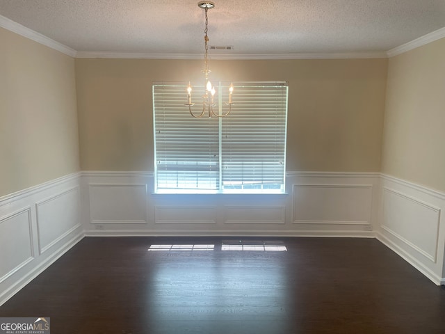 spare room with a textured ceiling, dark wood-type flooring, crown molding, and a notable chandelier