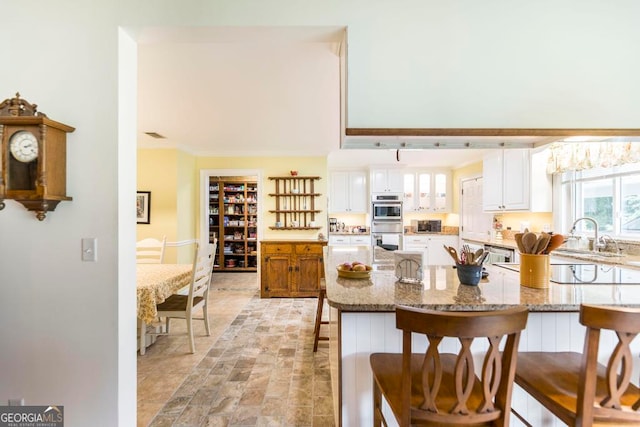 kitchen featuring light stone countertops, white cabinetry, sink, and a kitchen breakfast bar