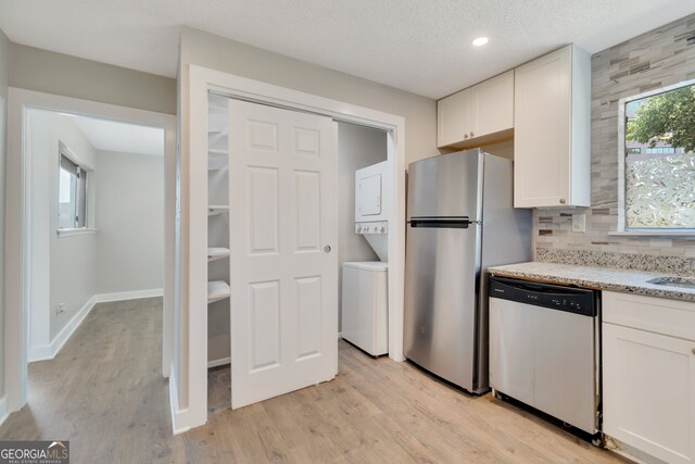 kitchen featuring stacked washer / drying machine, stainless steel appliances, white cabinets, light stone countertops, and light hardwood / wood-style floors