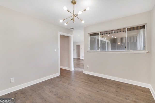 spare room with hardwood / wood-style flooring and a notable chandelier