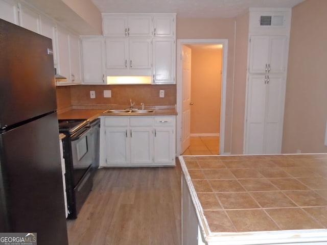 kitchen featuring white cabinetry, sink, tile counters, and stainless steel refrigerator