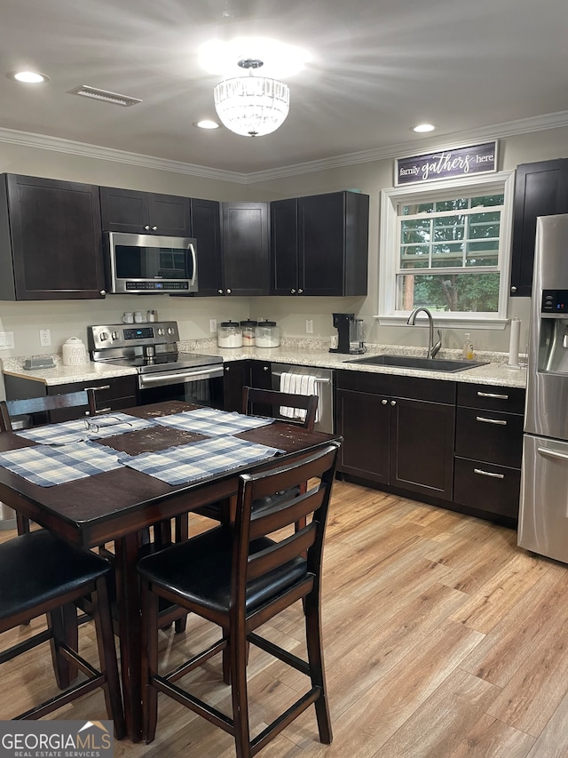 kitchen with crown molding, light stone counters, stainless steel appliances, light hardwood / wood-style floors, and sink