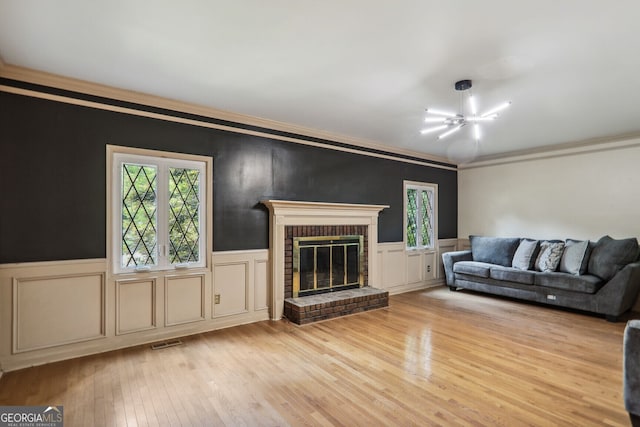 living room with a brick fireplace, light hardwood / wood-style floors, a notable chandelier, and ornamental molding