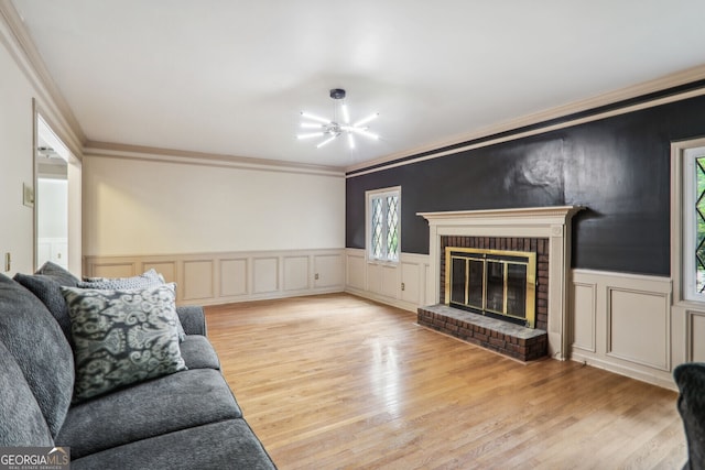 living room featuring a notable chandelier, a fireplace, crown molding, and light hardwood / wood-style flooring