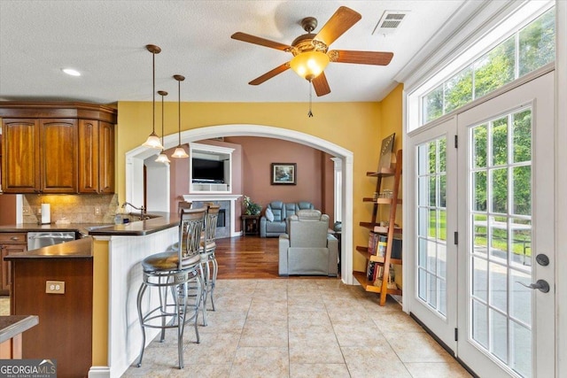 kitchen featuring decorative light fixtures, backsplash, dishwasher, a breakfast bar area, and light tile patterned floors