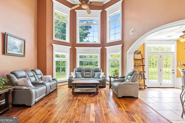 living room featuring ceiling fan, wood-type flooring, a towering ceiling, crown molding, and a healthy amount of sunlight