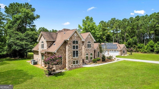 rear view of property with central air condition unit, solar panels, a yard, and a garage