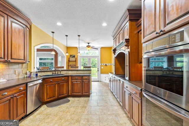 kitchen with a textured ceiling, appliances with stainless steel finishes, decorative light fixtures, tasteful backsplash, and sink