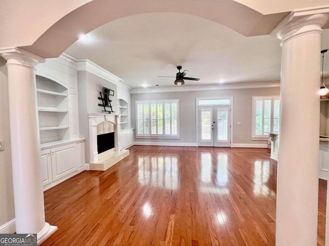 unfurnished living room featuring wood-type flooring, ornamental molding, ceiling fan, and decorative columns