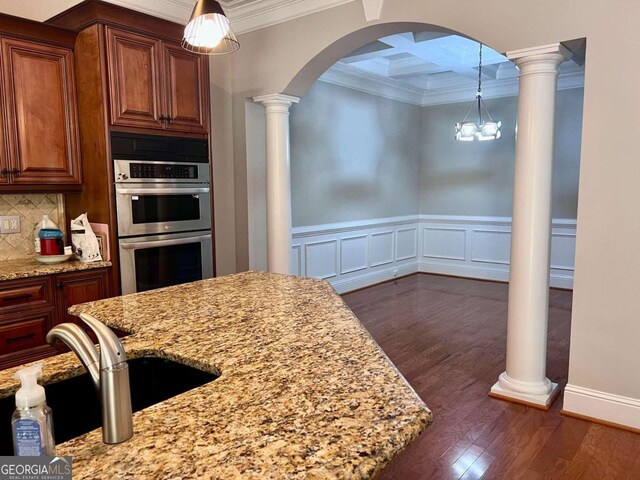 kitchen featuring light stone countertops, ornamental molding, dark hardwood / wood-style flooring, stainless steel double oven, and backsplash