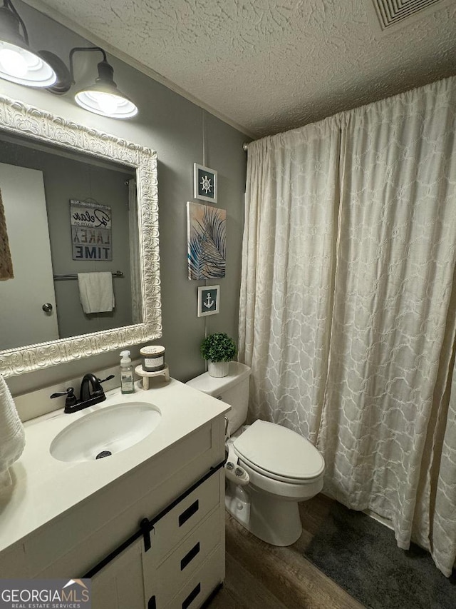 bathroom with hardwood / wood-style flooring, toilet, vanity, and a textured ceiling