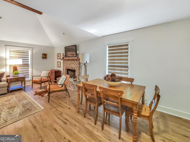 dining room with a fireplace, vaulted ceiling, and light hardwood / wood-style flooring