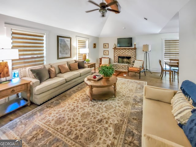 living room with wood-type flooring, ceiling fan, a brick fireplace, and lofted ceiling