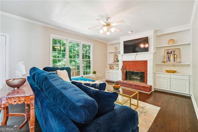 living room with crown molding, built in shelves, a brick fireplace, ceiling fan, and dark hardwood / wood-style floors