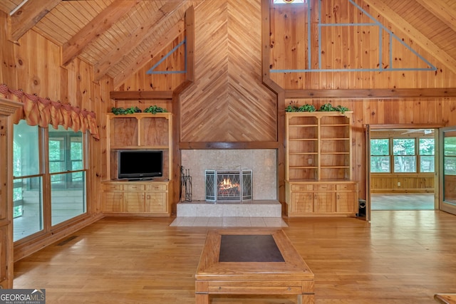 unfurnished living room featuring a tiled fireplace, wood walls, beamed ceiling, and high vaulted ceiling