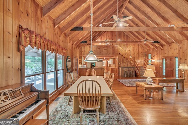 dining area with beam ceiling, light hardwood / wood-style flooring, high vaulted ceiling, wood walls, and wood ceiling