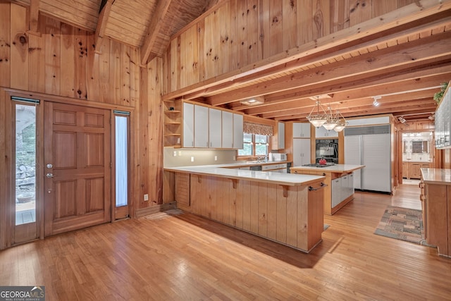 kitchen featuring a kitchen bar, kitchen peninsula, wood walls, and beamed ceiling