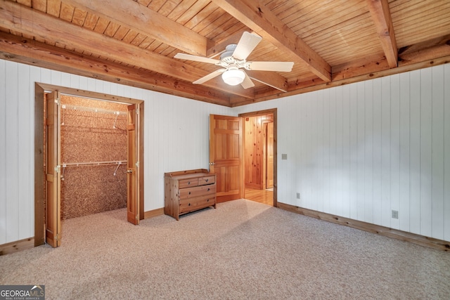 unfurnished bedroom with a walk in closet, ceiling fan, beamed ceiling, a closet, and wood walls