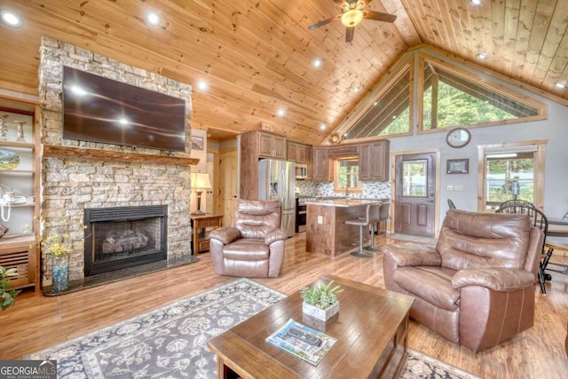 living room with wooden ceiling, light wood-type flooring, ceiling fan, a stone fireplace, and high vaulted ceiling