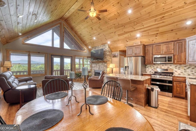 dining space with light wood-type flooring, wooden ceiling, high vaulted ceiling, and a stone fireplace