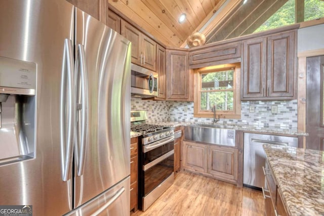 kitchen featuring light stone countertops, vaulted ceiling, stainless steel appliances, light wood-type flooring, and backsplash