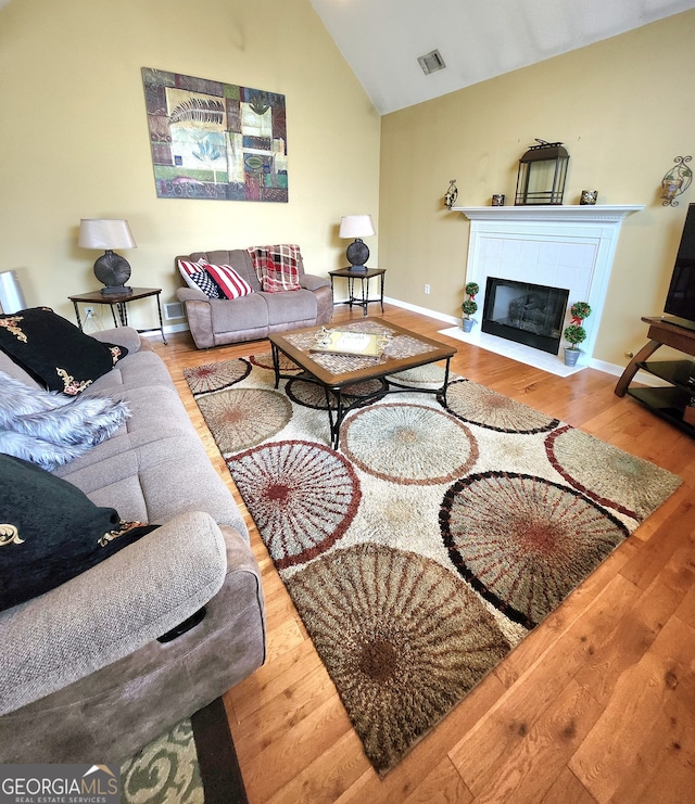 living room featuring vaulted ceiling, light wood-type flooring, and a tile fireplace