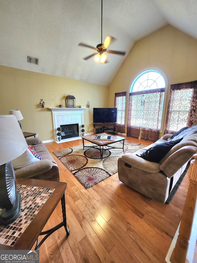 living room featuring a tiled fireplace, ceiling fan, a textured ceiling, hardwood / wood-style flooring, and vaulted ceiling