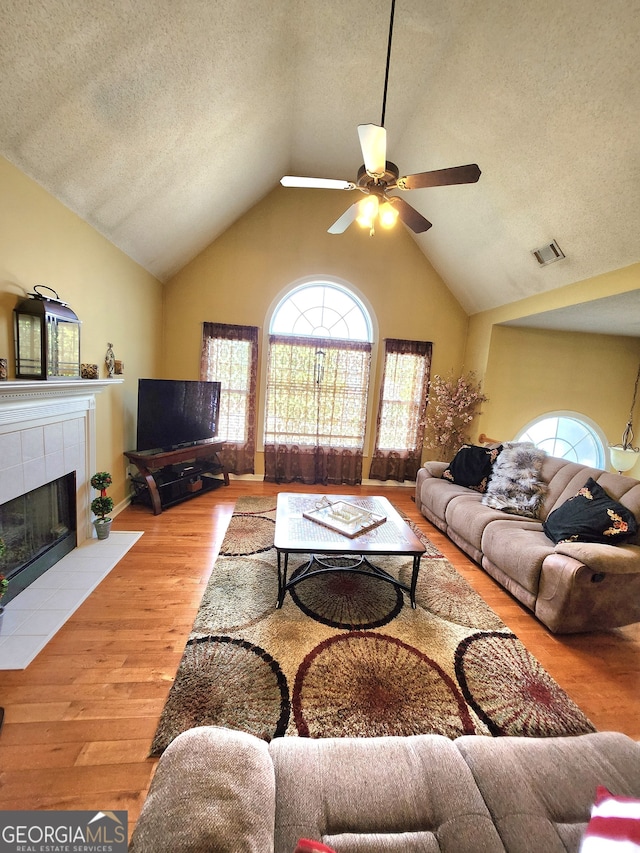 living room featuring light hardwood / wood-style flooring, vaulted ceiling, a textured ceiling, a fireplace, and ceiling fan