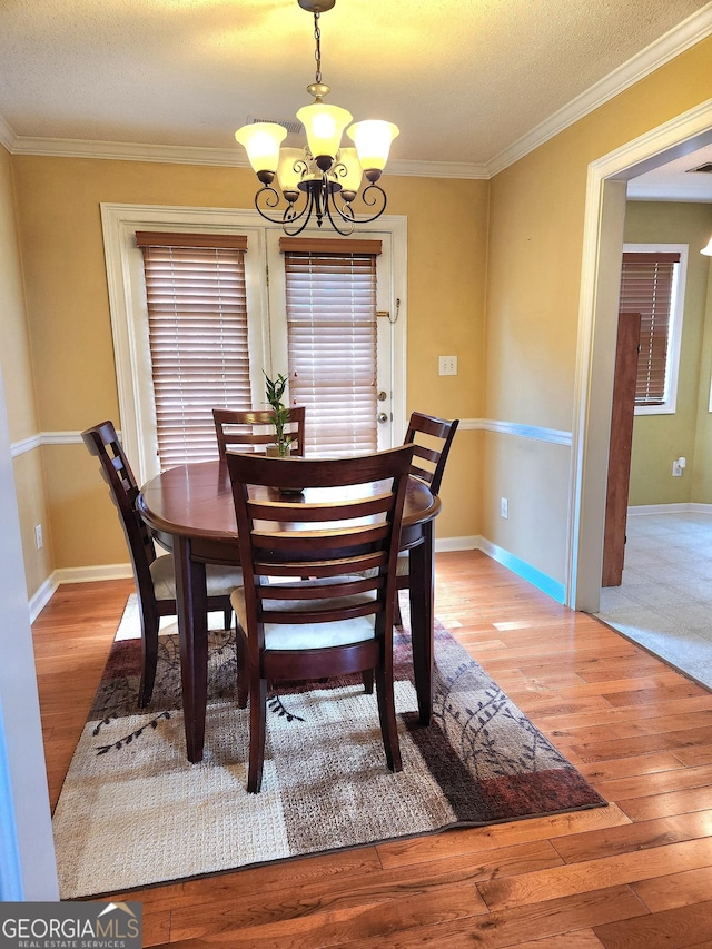 dining area featuring a chandelier, hardwood / wood-style flooring, ornamental molding, a textured ceiling, and baseboards