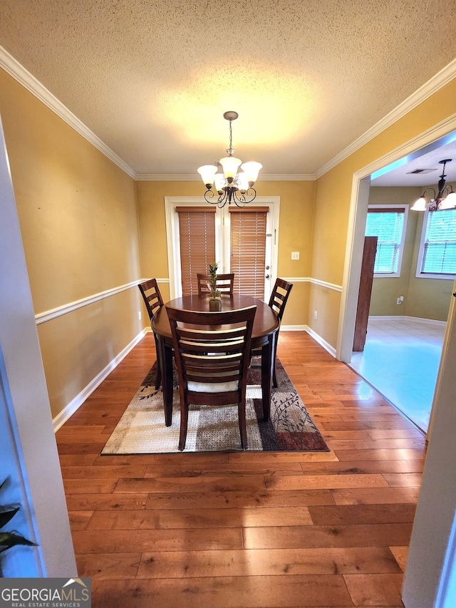 dining space with a notable chandelier, hardwood / wood-style flooring, a textured ceiling, and ornamental molding