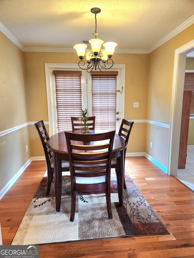 dining room featuring an inviting chandelier, ornamental molding, a textured ceiling, and light wood-type flooring