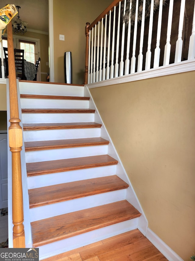 staircase with crown molding, a notable chandelier, and hardwood / wood-style flooring