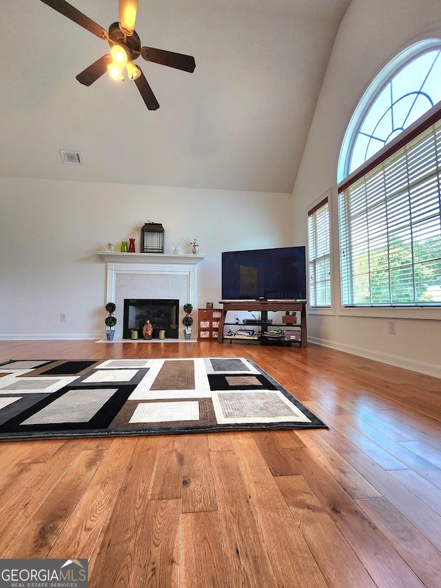unfurnished living room with wood-type flooring, high vaulted ceiling, baseboards, a ceiling fan, and a tile fireplace