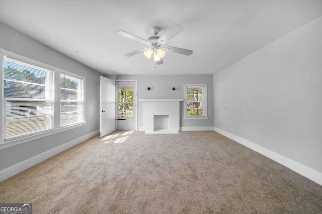 unfurnished living room featuring a wealth of natural light, carpet flooring, a brick fireplace, and ceiling fan