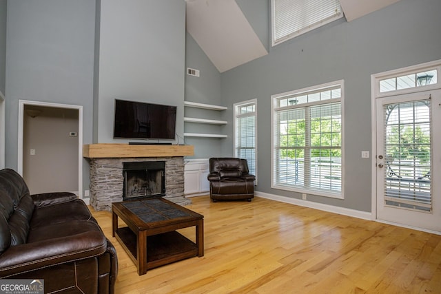 living room featuring a fireplace, a towering ceiling, light hardwood / wood-style floors, and built in features