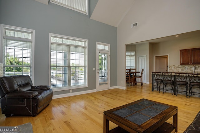 living room featuring plenty of natural light, light wood-type flooring, and high vaulted ceiling