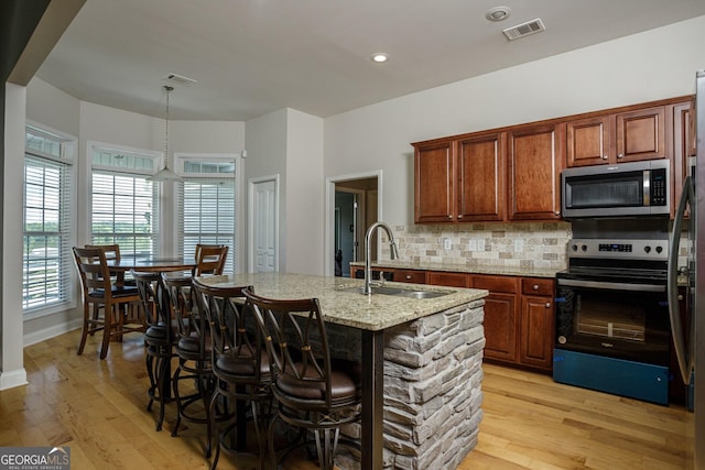 kitchen featuring a kitchen island with sink, sink, stainless steel appliances, and light wood-type flooring