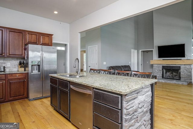 kitchen with sink, light hardwood / wood-style flooring, an island with sink, a fireplace, and appliances with stainless steel finishes