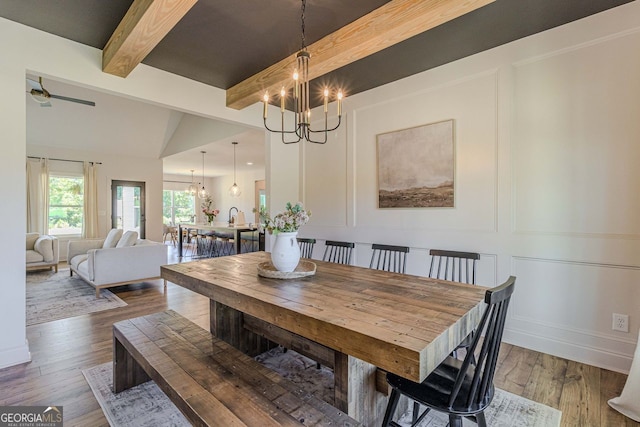 dining area featuring sink, ceiling fan with notable chandelier, hardwood / wood-style flooring, and vaulted ceiling with beams