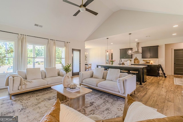 living room with light hardwood / wood-style floors, sink, high vaulted ceiling, and ceiling fan