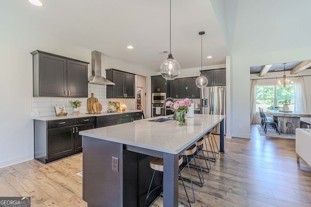 kitchen featuring decorative backsplash, a kitchen island with sink, light hardwood / wood-style floors, and wall chimney exhaust hood