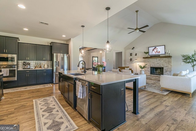 kitchen featuring a fireplace, sink, a center island with sink, light hardwood / wood-style floors, and appliances with stainless steel finishes