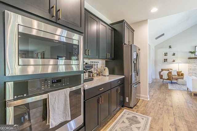 kitchen featuring appliances with stainless steel finishes, lofted ceiling, light wood-type flooring, and dark brown cabinetry