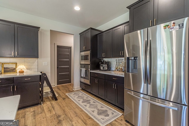 kitchen featuring light wood-type flooring, light stone countertops, stainless steel appliances, and backsplash