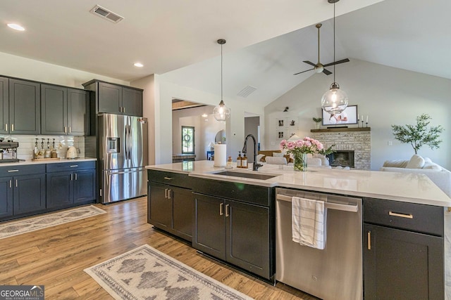 kitchen featuring ceiling fan, decorative backsplash, appliances with stainless steel finishes, light hardwood / wood-style flooring, and a stone fireplace